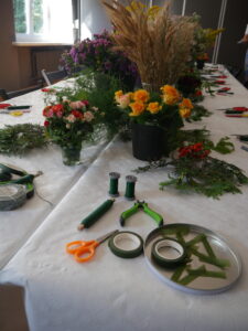 Stół, a na nim wiaderka pełne kwiatów oraz leżące obok nożyczki, tasiemki, nici.